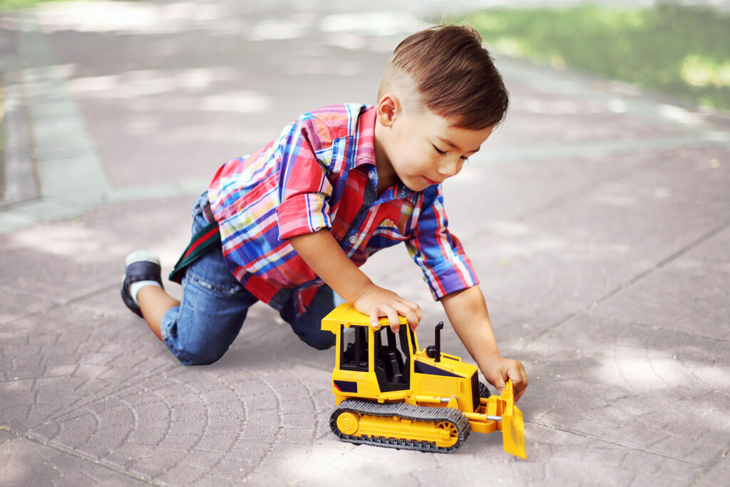 young boy playing with bulldozer toy outside